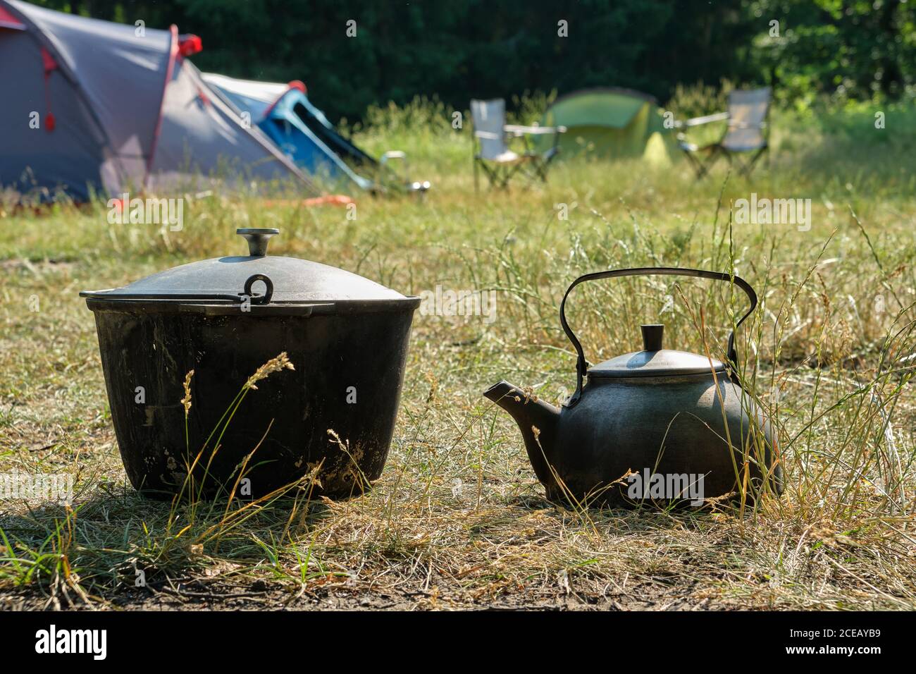 Tourist camp. A kettle and a tourist cooking pot. Camping tents and folding chairs on background. Stock Photo
