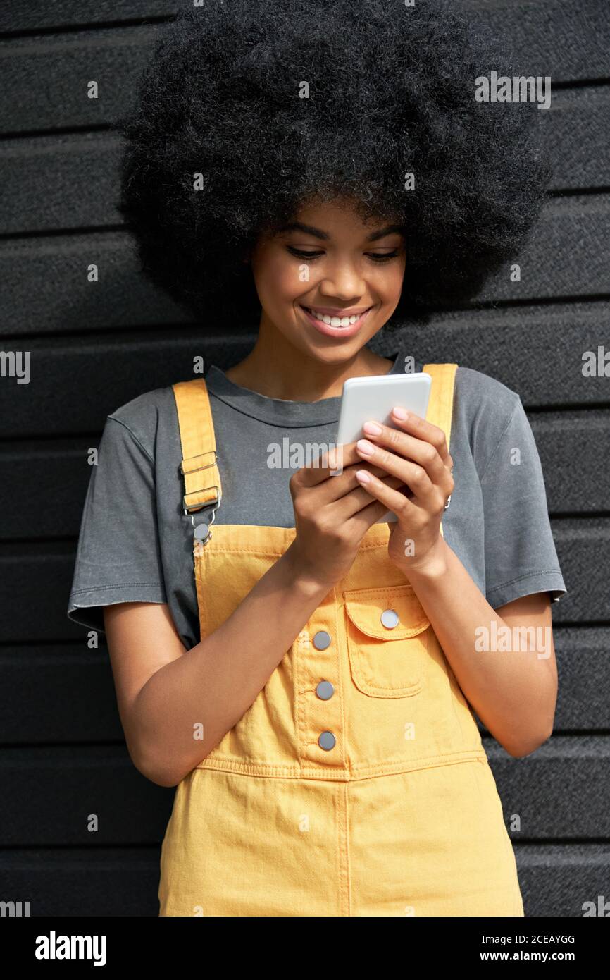 Smiling African young hipster lady with Afro hair using smartphone. Stock Photo