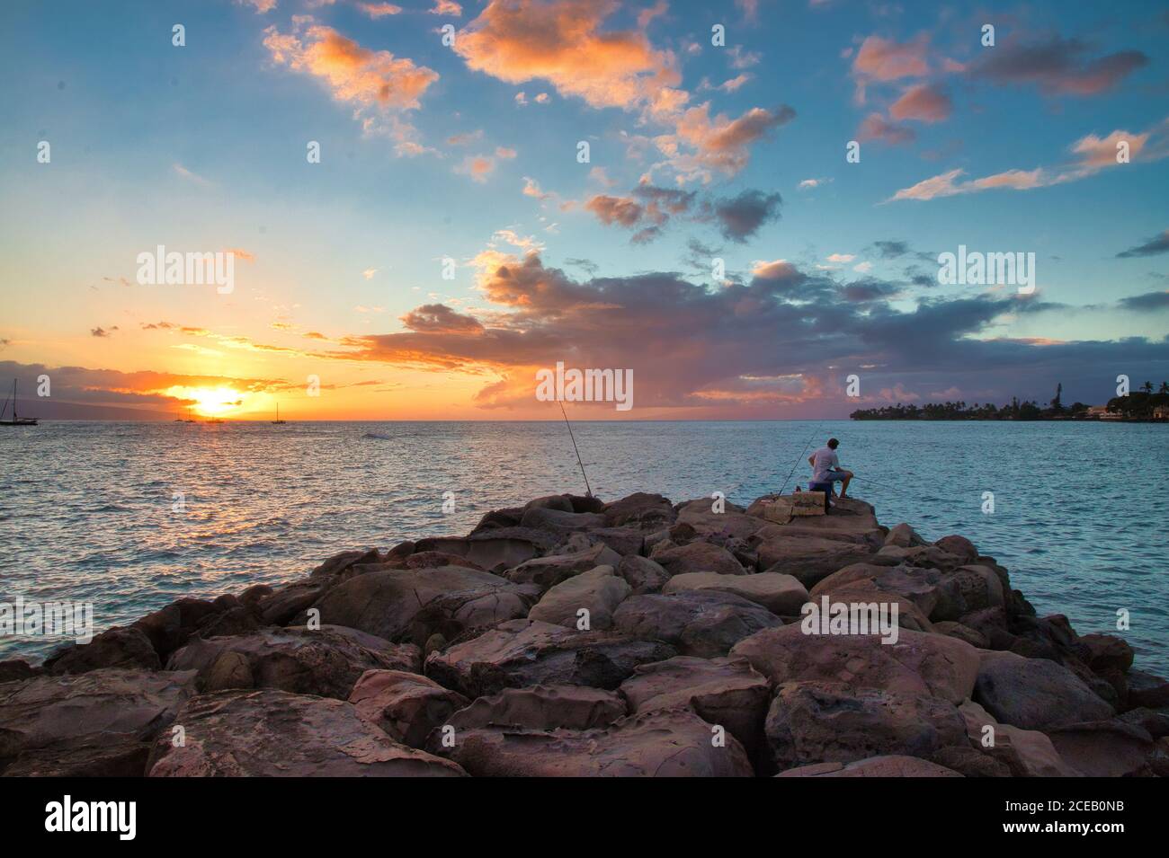 Unrecognizable,silhoueeted people on the breakwall in Lahaina at sunset. Stock Photo