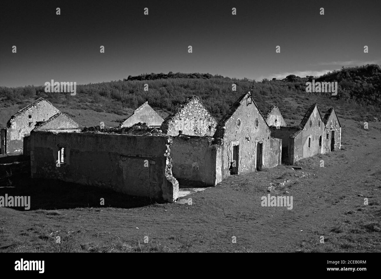 Abandoned half ruined buildings made of stone standing in vast field in black and white colors Stock Photo