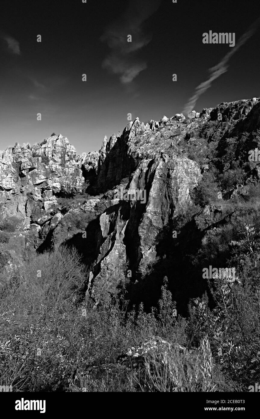 High steep sharp rocks with trees growing at bottom on background of sky in black and white colors Stock Photo