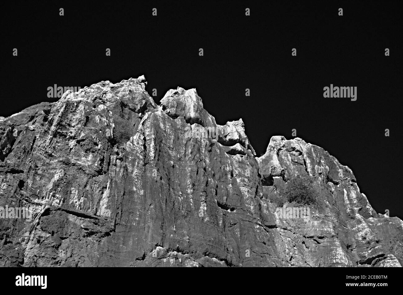 High steep sharp rocks with trees growing at bottom on background of sky in black and white colors Stock Photo