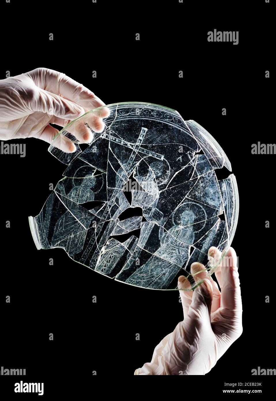 Person in plastic gloves holding broken antique dish with religious picture isolated on black background Stock Photo