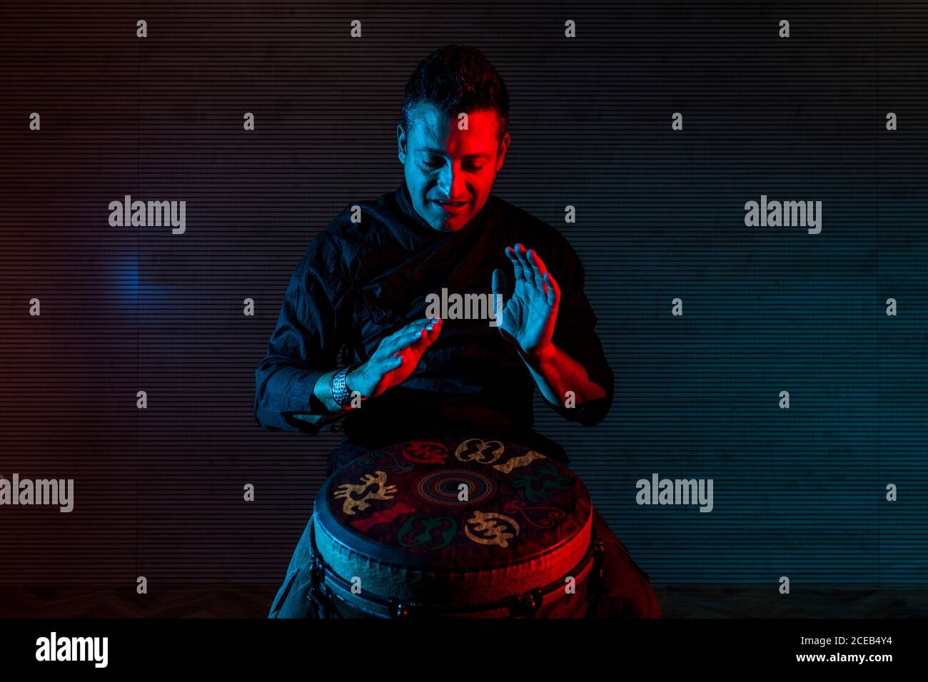 Young percussionist practicing technique with the tam tam or drum, colored lighting in red and blue. Stock Photo