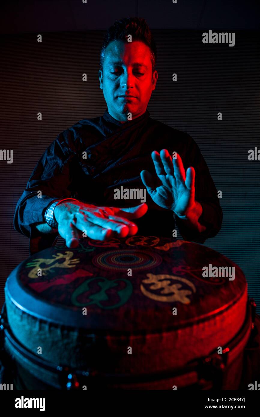 Young percussionist practicing technique with the tam tam or drum, colored lighting in red and blue. Stock Photo