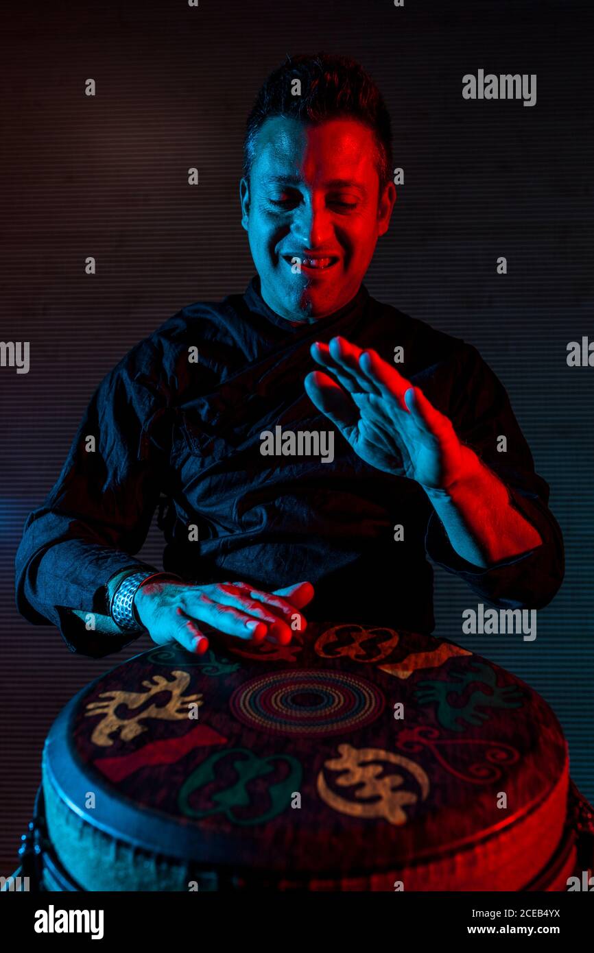 Young percussionist practicing technique with the tam tam or drum, colored lighting in red and blue. Stock Photo
