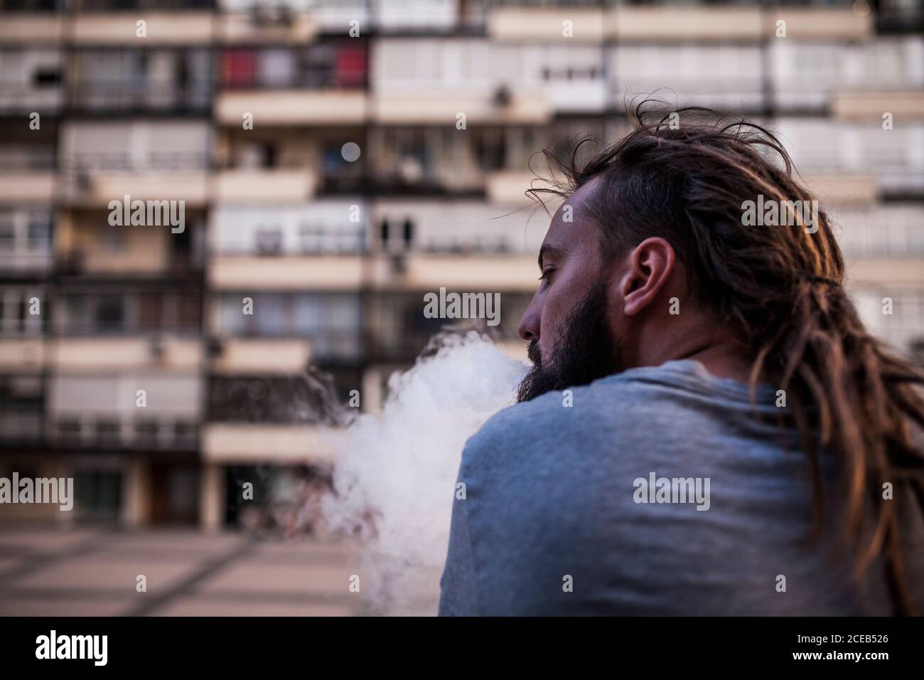 young and Caucasian Rastafarian man smoking and exposing smoke from behind and look left Stock Photo