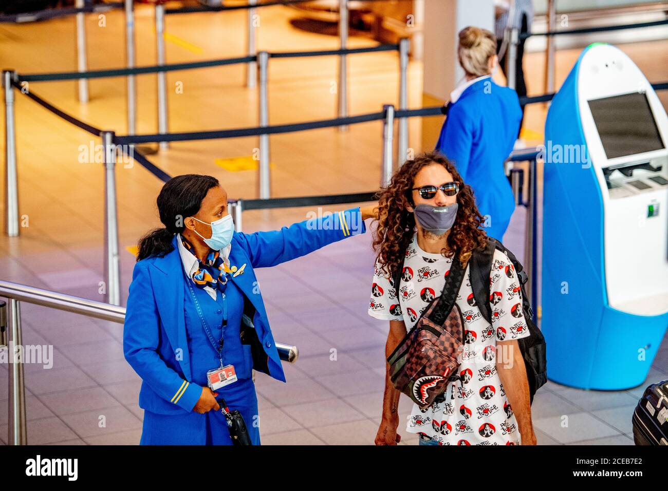 A KLM stewardess wearing a face mask directs a traveller at the airport.It  is business again at Schiphol Airport as people travel during the summer  holidays however with mandatory wearing of facemasks.