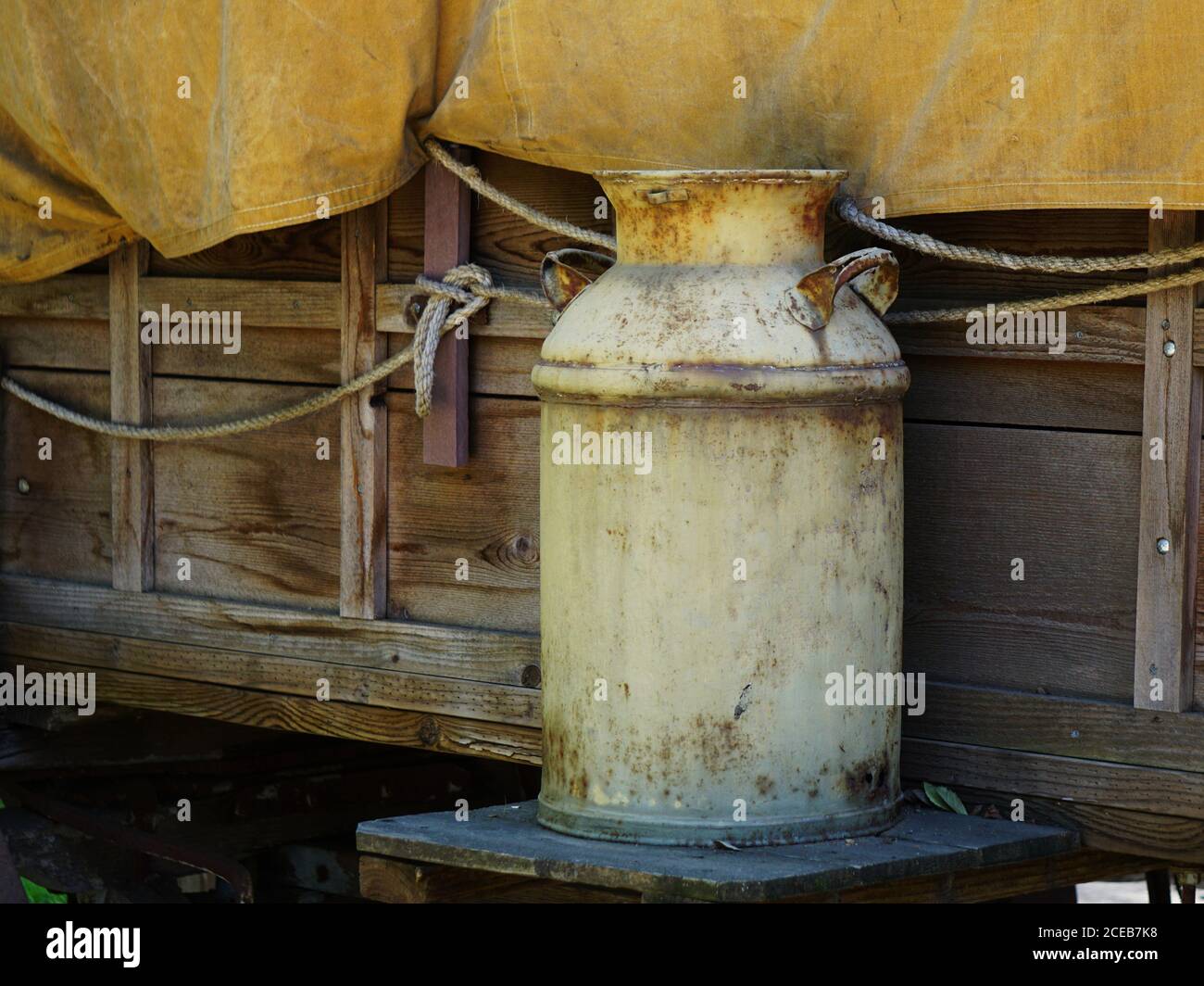 Old rusty milk can sitting outside a covered wagon. Stock Photo