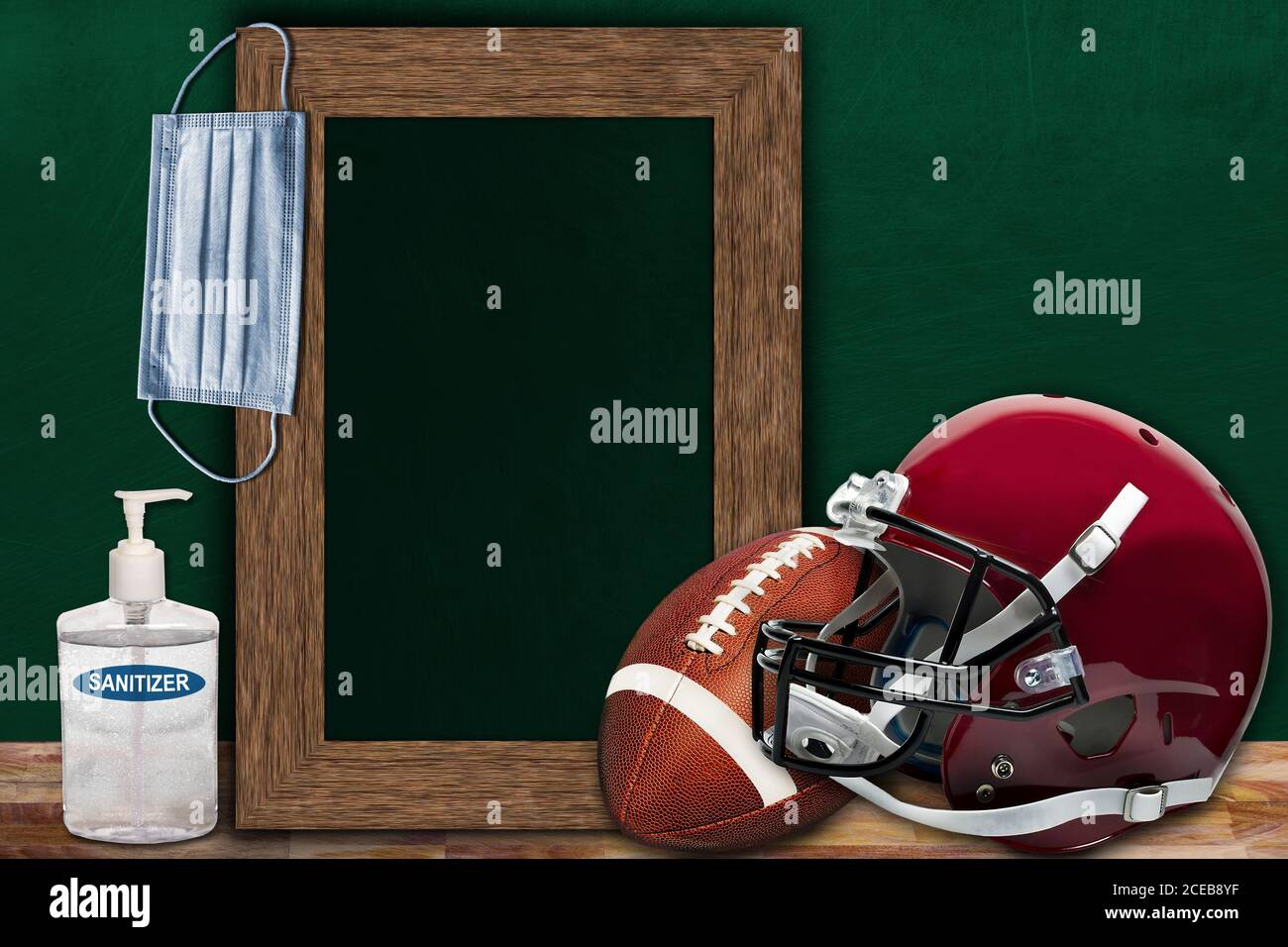 COVID-19 new normal sports concept in a classroom setting showing framed chalkboard with copy space and American football and helmet on wooden table. Stock Photo