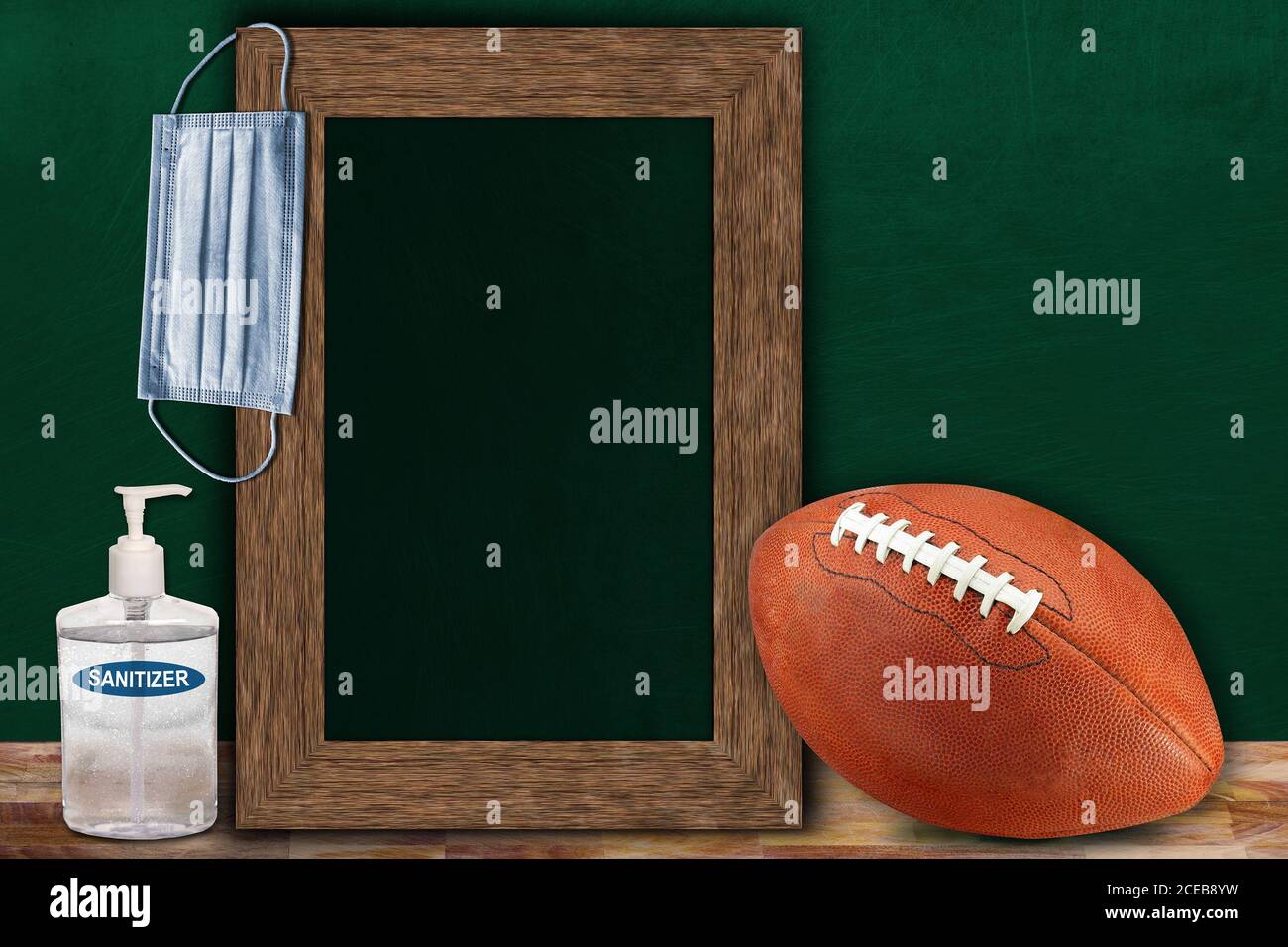 COVID-19 new normal sports concept in a classroom setting showing framed chalkboard with copy space and American football on wooden table. Stock Photo