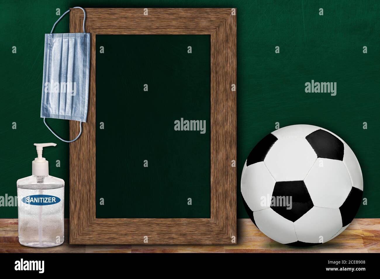COVID-19 new normal sports concept in a classroom setting showing framed chalkboard with copy space and soccer ball on wooden table. Stock Photo