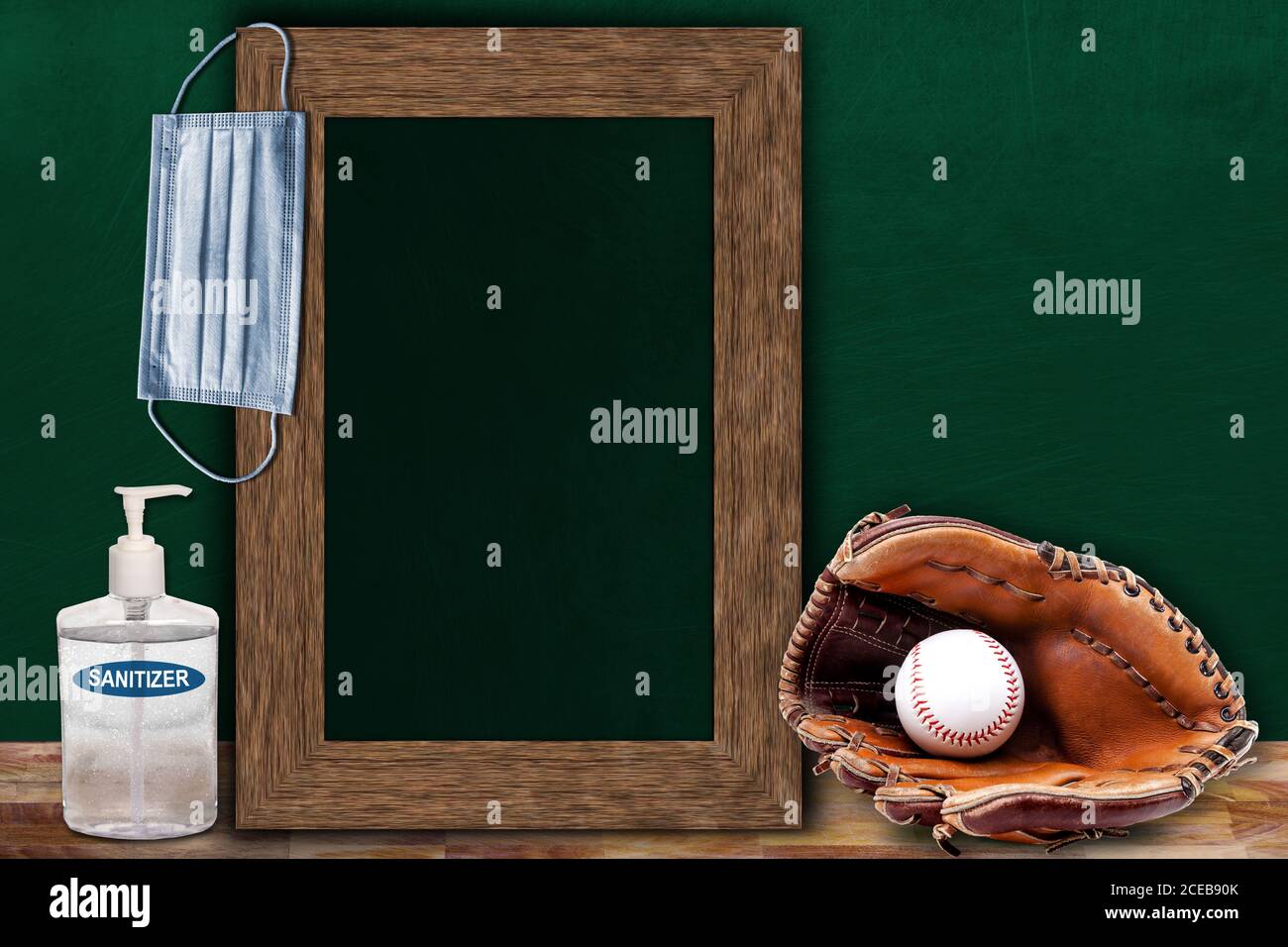 COVID-19 new normal sports concept in a classroom setting showing framed chalkboard with copy space and baseball glove and ball on wooden table. Stock Photo