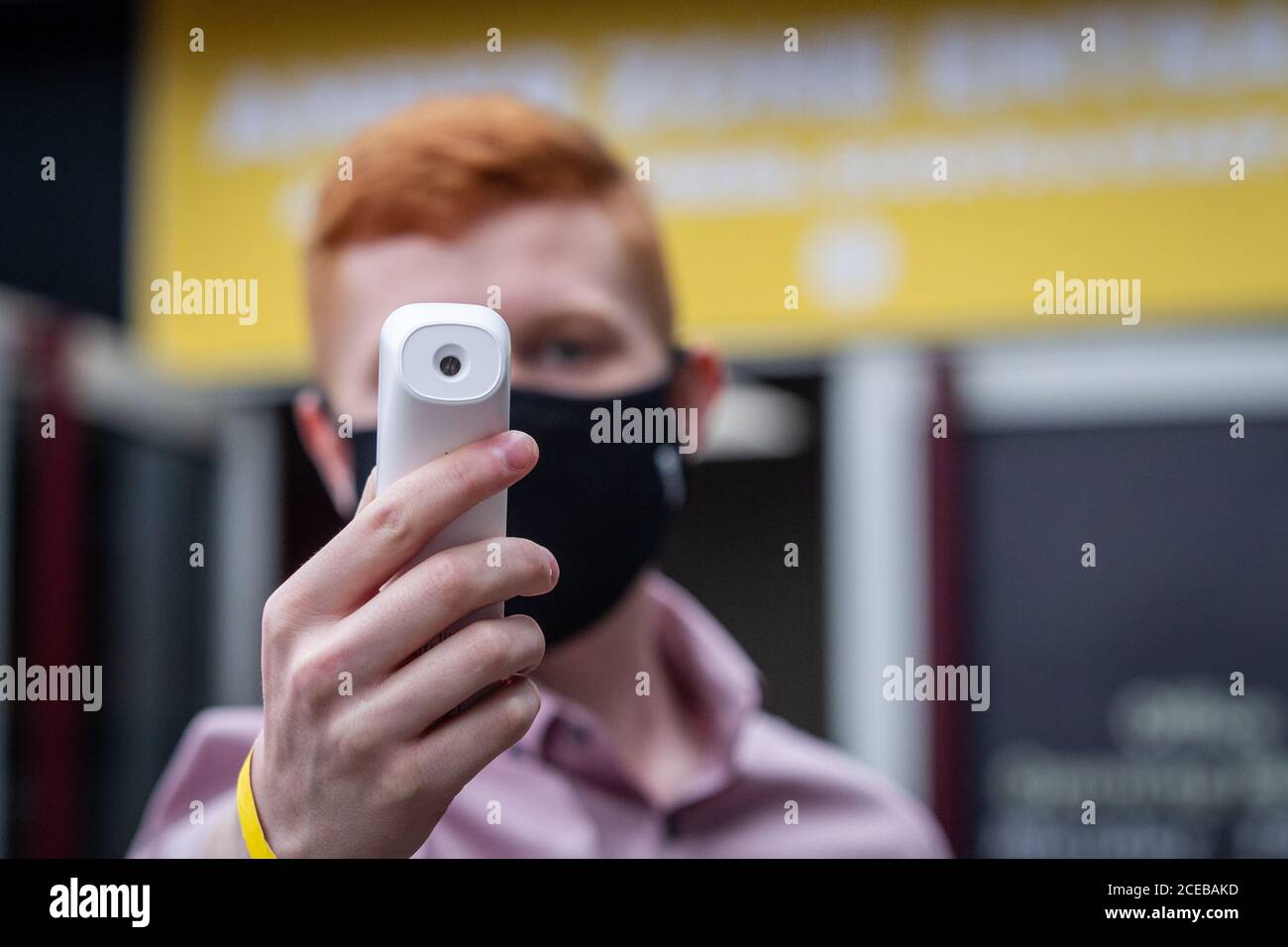 Forehead non-contact thermometer being used to check body temperature as people enter sports stadium during Coronavirus pandemic in UK Stock Photo