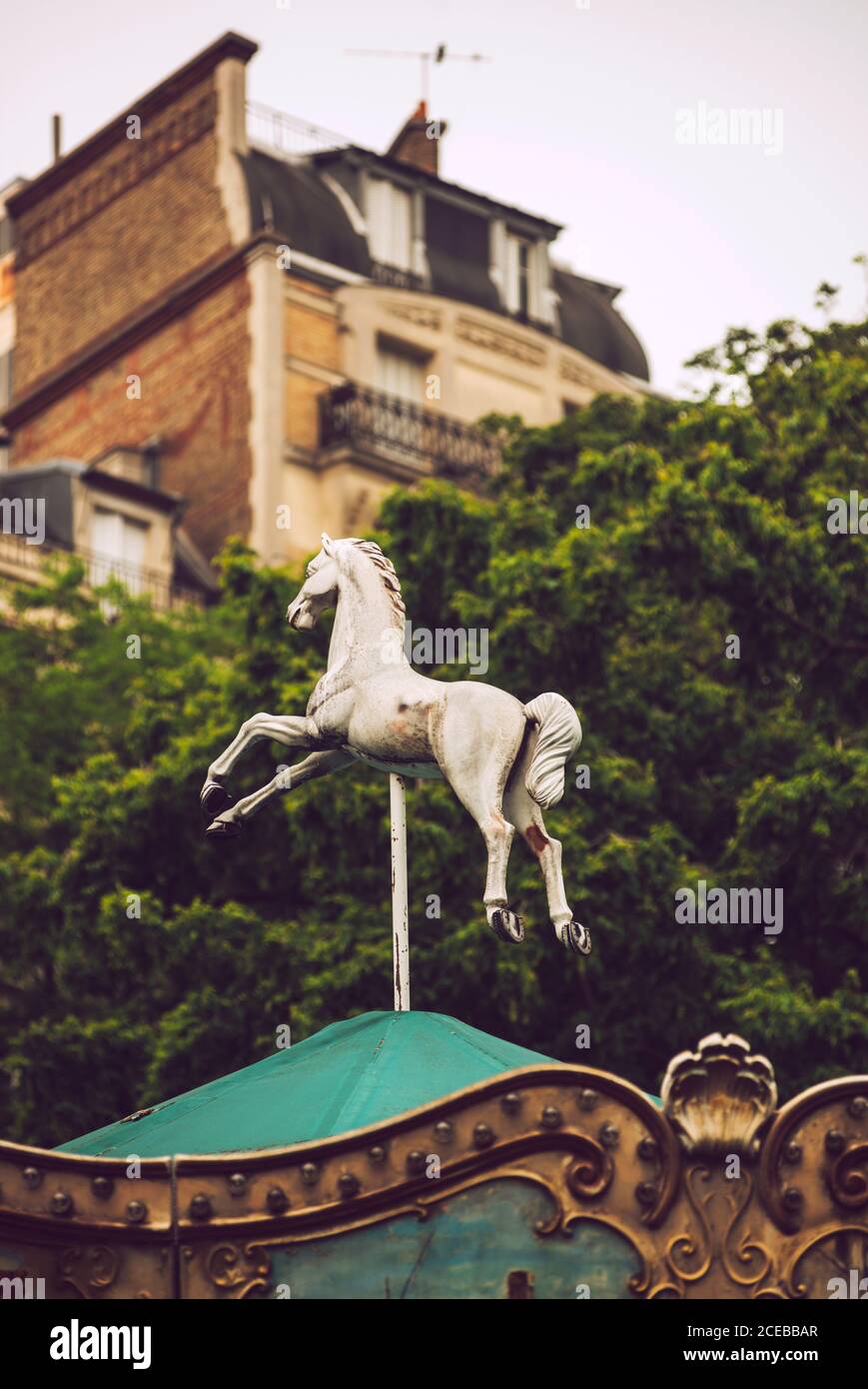 Close up view of white horse statue on green rooftop on background of trees and stone building in Paris Stock Photo