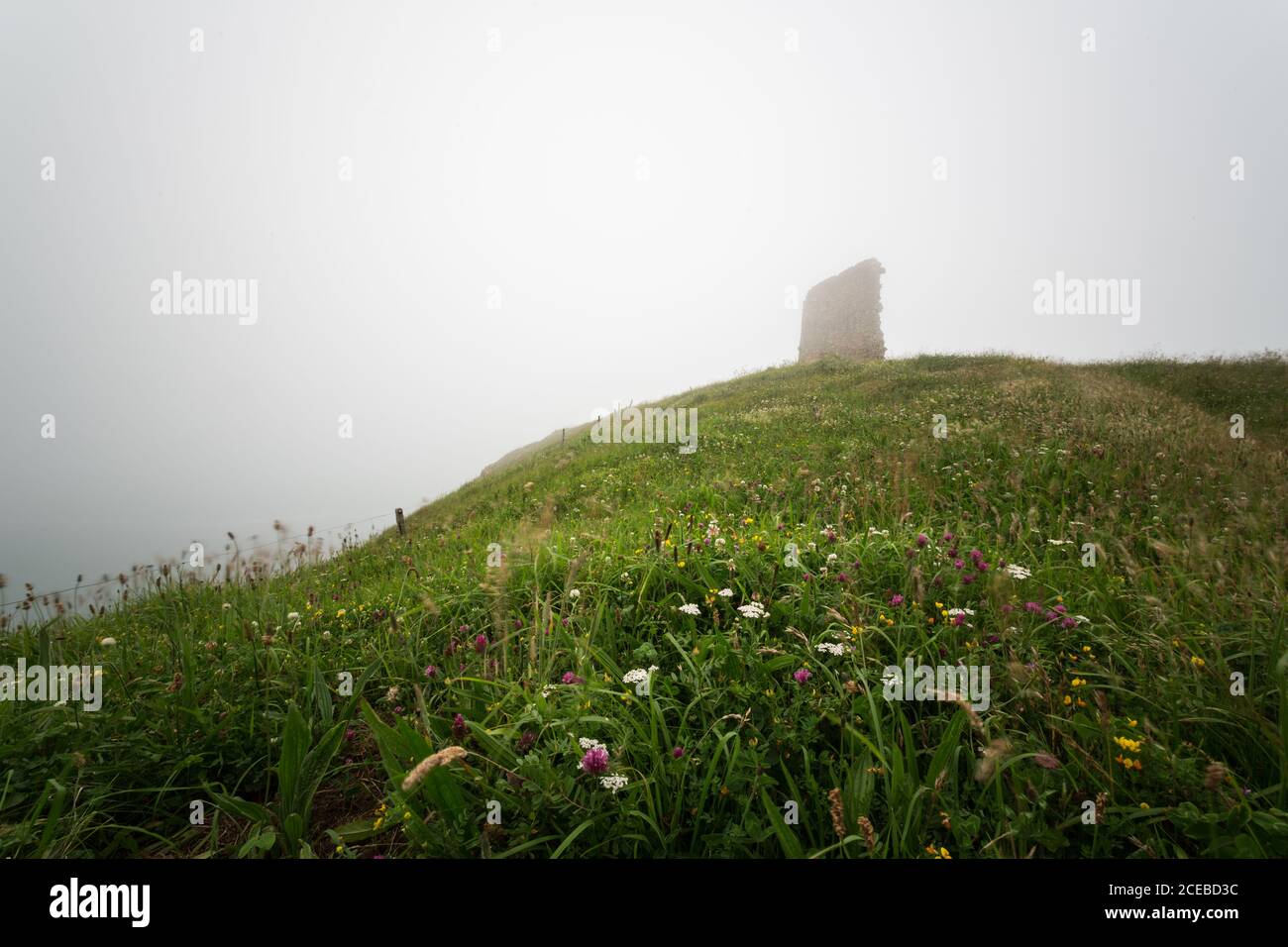 Spectacular view of vague structure on top of grassy hill on foggy day Stock Photo