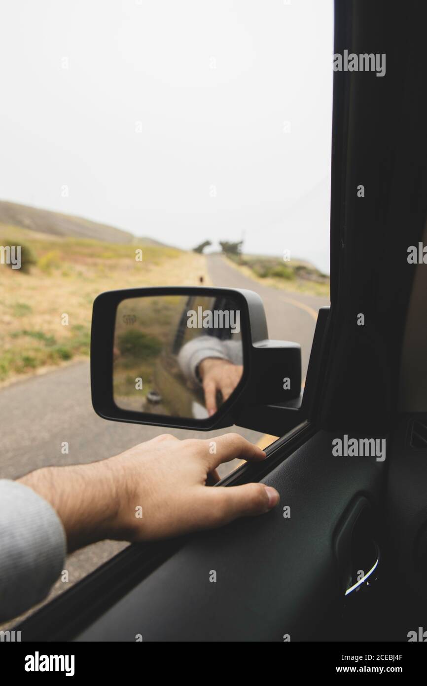 Hand of anonymous man lying on car window near wing mirror during amazing trip through beautiful countryside Stock Photo
