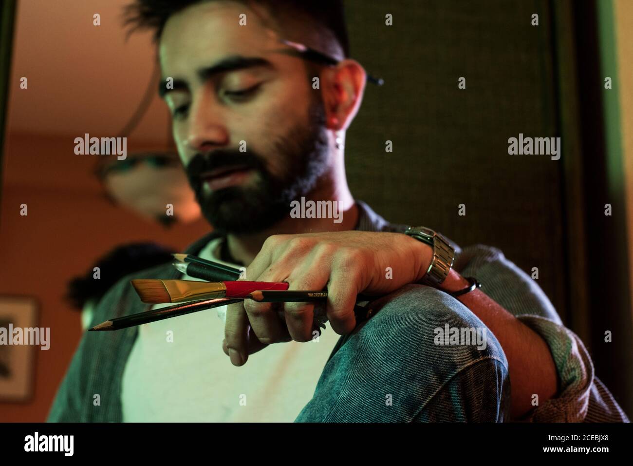 Thoughtful adult artist man sitting with pencils and brush at home. Stock Photo