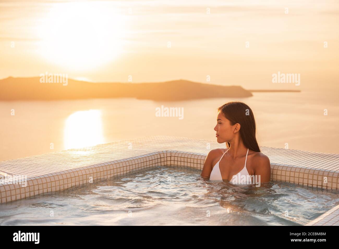 Luxury resort woman swimming in jacuzzi hot tub outside on private hotel room balcony watching sunset over Mediterranean sea. Europe honeymoon Stock Photo