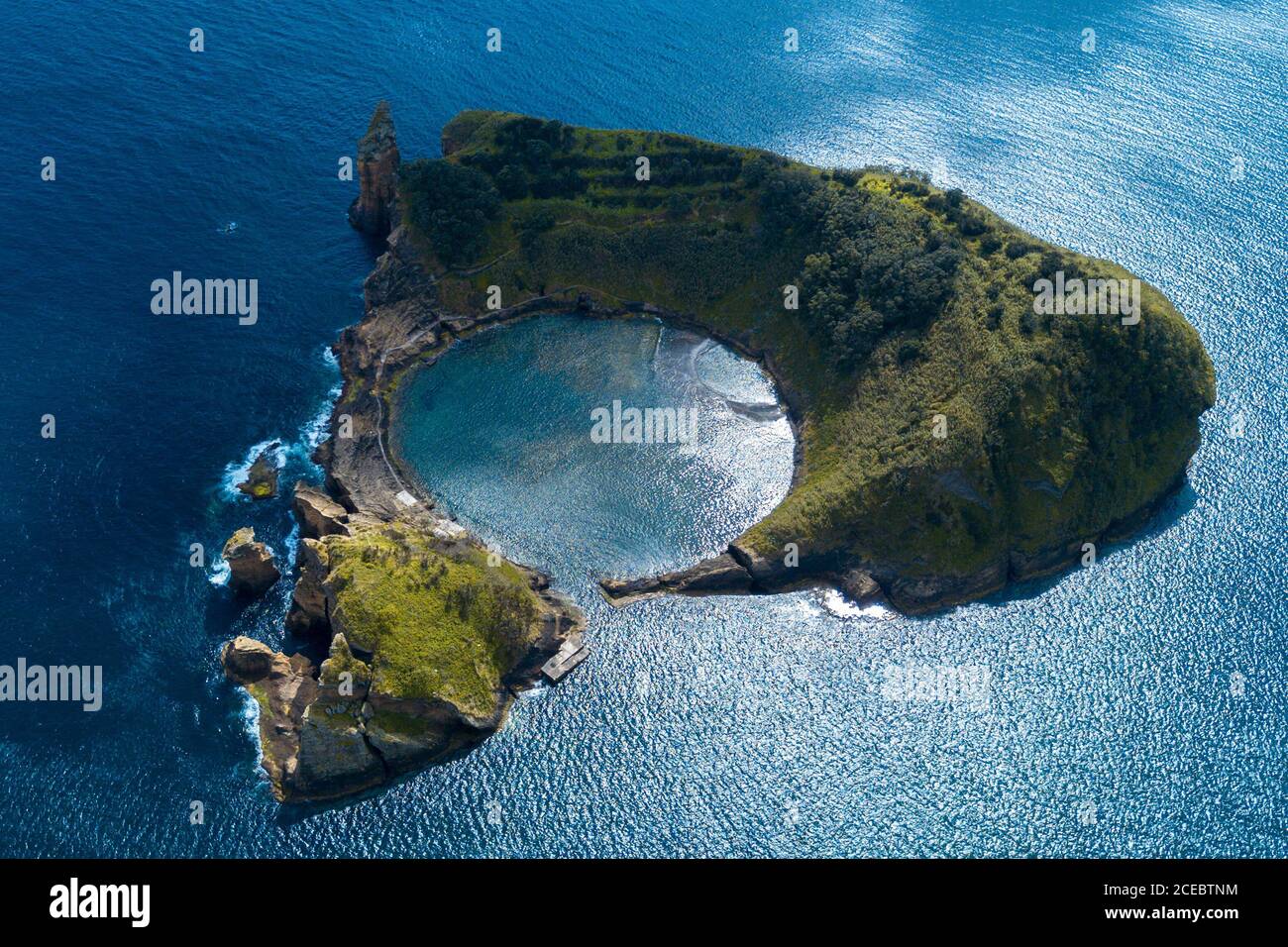 Aerial view of stunning small triangular island with trees and cliffs surrounded by calm ocean with amazing circular bay on sunny summer day Stock Photo