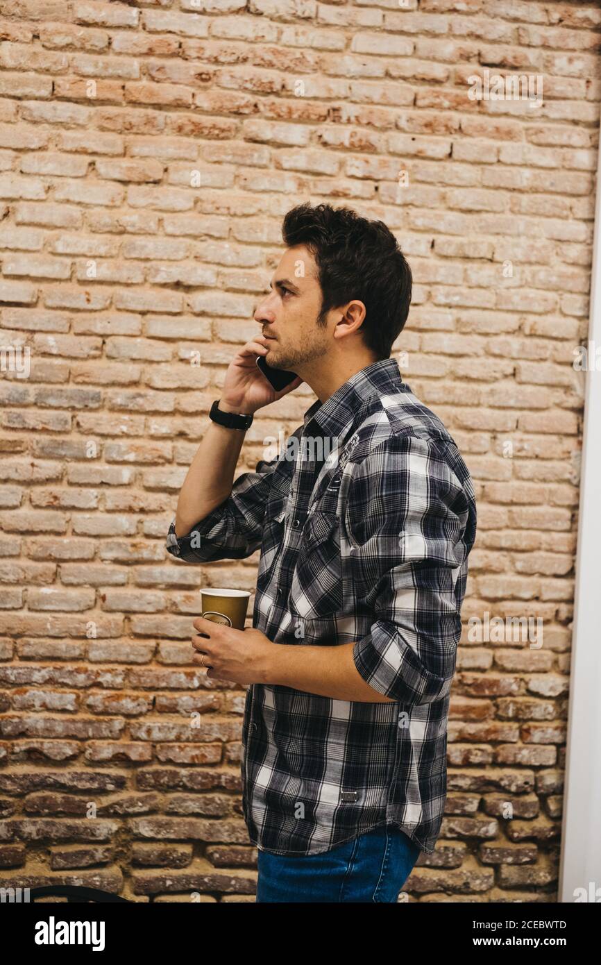 Young man with cup talking on smartphone Stock Photo