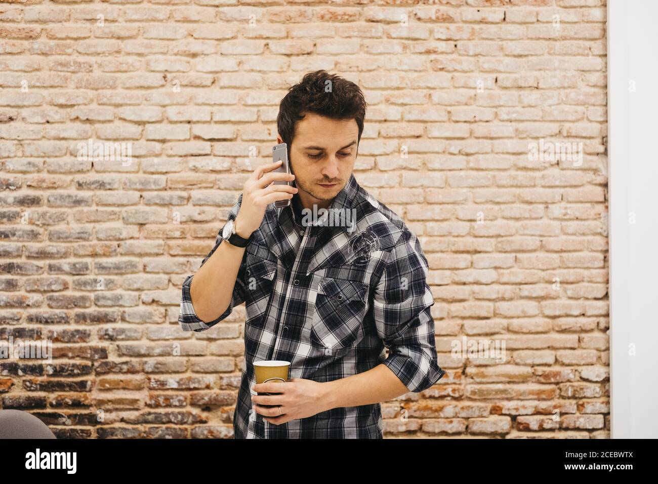 Young man with cup talking on smartphone Stock Photo