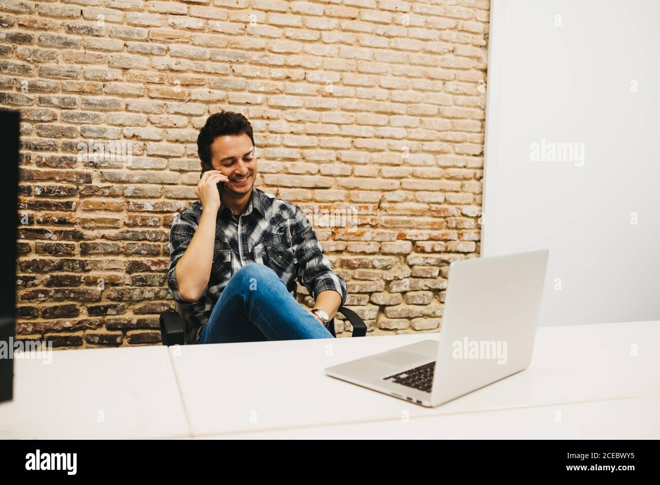 Young man using smartphone at table with laptop Stock Photo