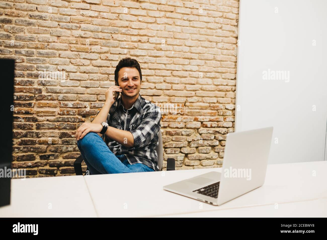 Young man using smartphone at table with laptop Stock Photo