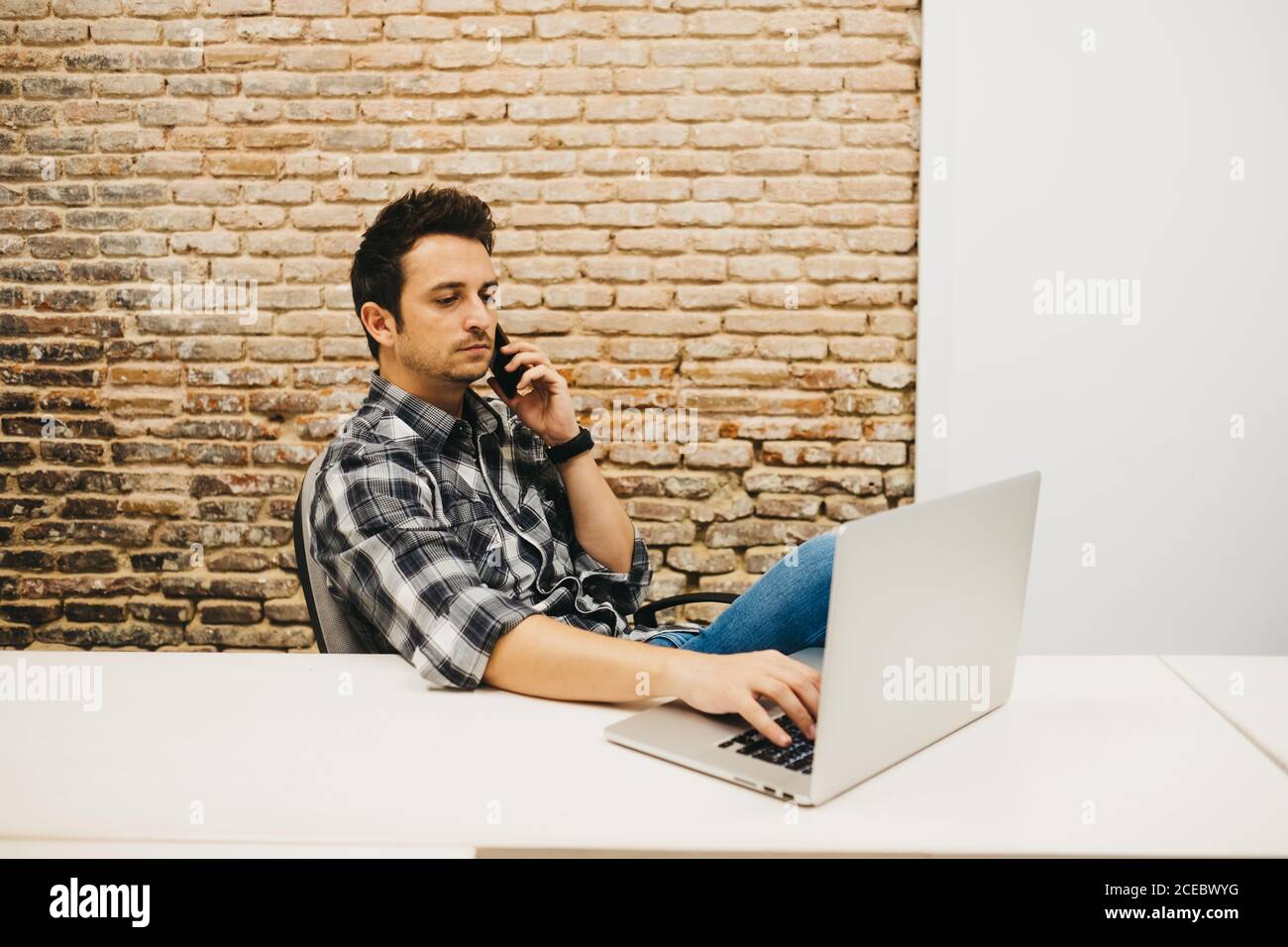 Young man using smartphone at table with laptop Stock Photo