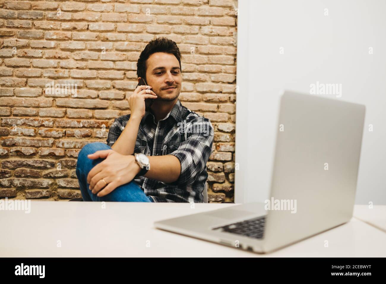 Young man using smartphone at table with laptop Stock Photo