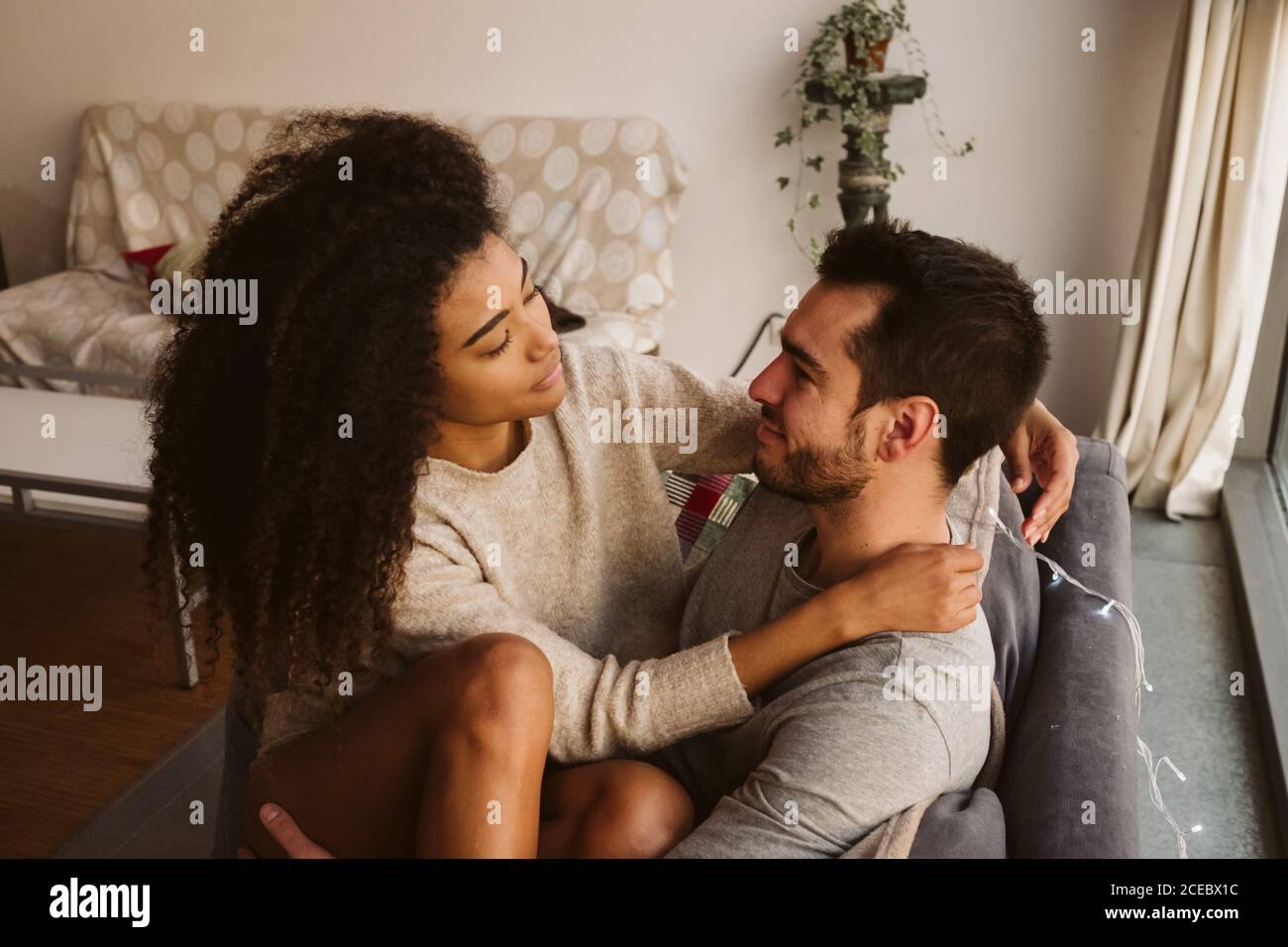 Young multiracial couple hugging on sofa Stock Photo