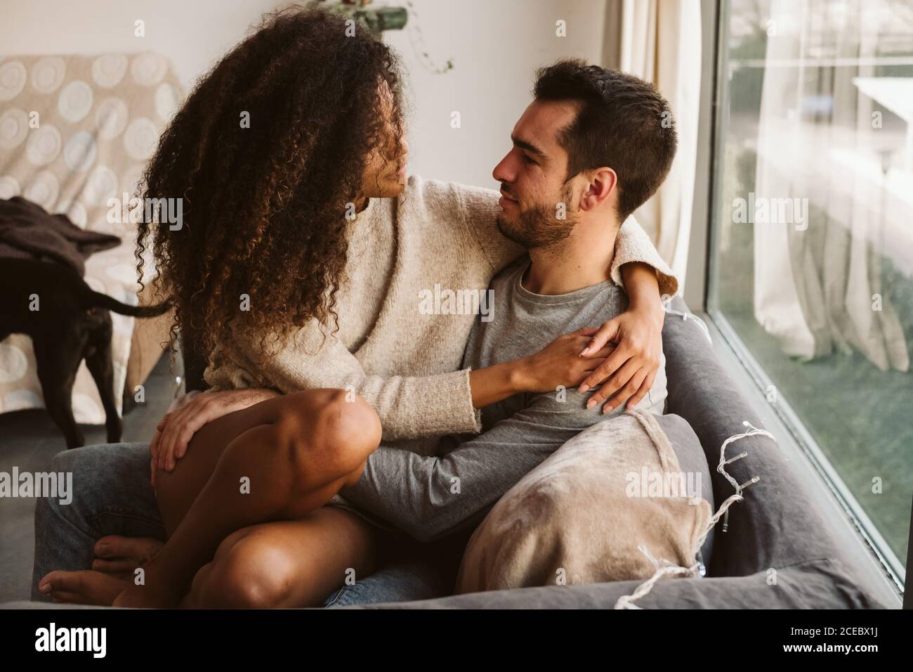 Young multiracial couple hugging on sofa Stock Photo