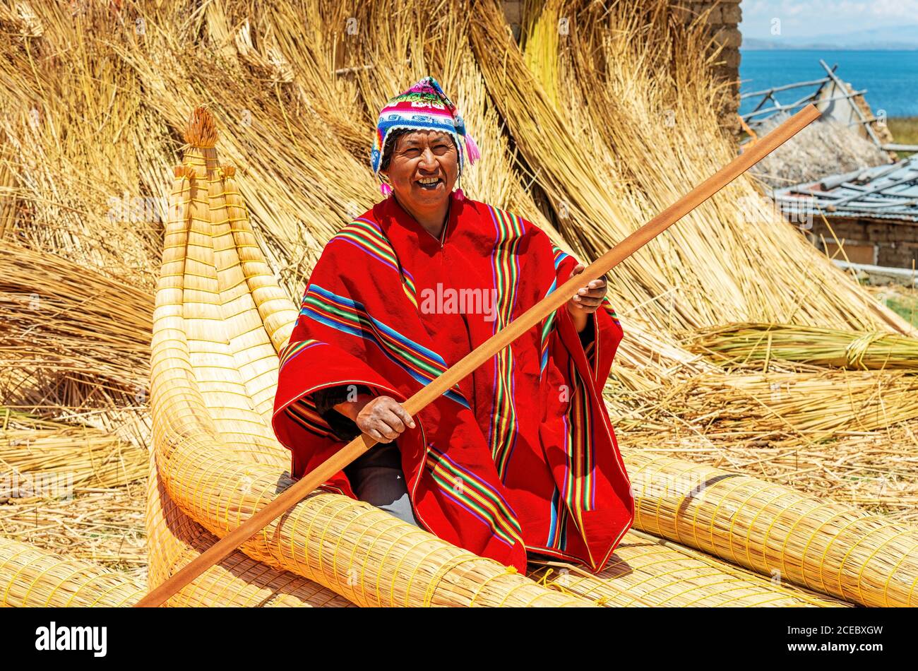 A smiling Aymara indigenous man in a red poncho doing a demonstration on how row a totora reed boat, Titicaca Lake, Bolivia. Stock Photo