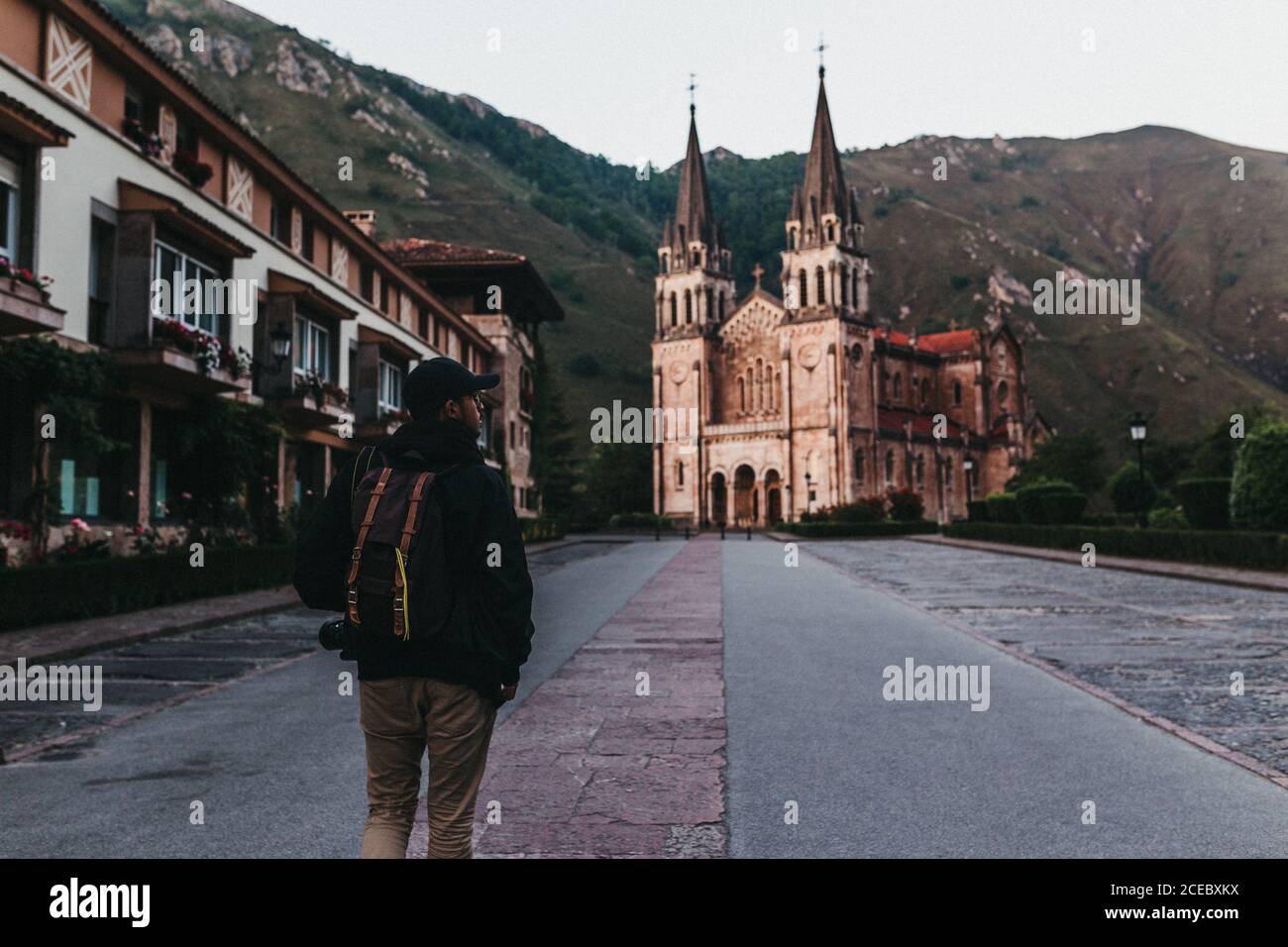 Back view of man with backpack walking on street of small mountain town towards beautiful church Stock Photo