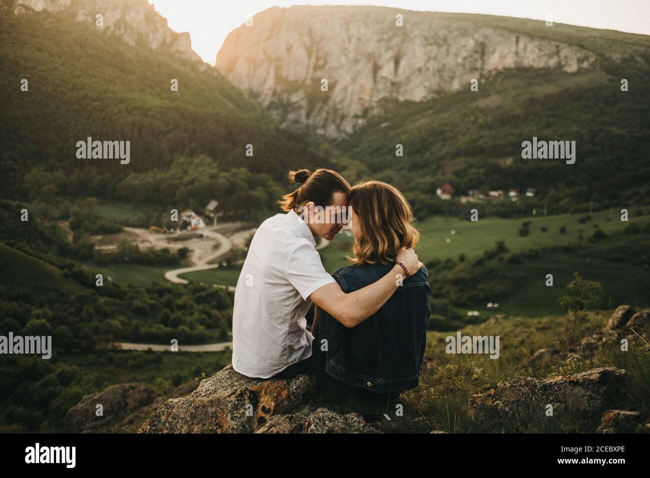 Cute couple hugging and toughing foreheads while sitting on rocky slope on  background of beautiful valley and mountains Stock Photo - Alamy, image size:1300x956