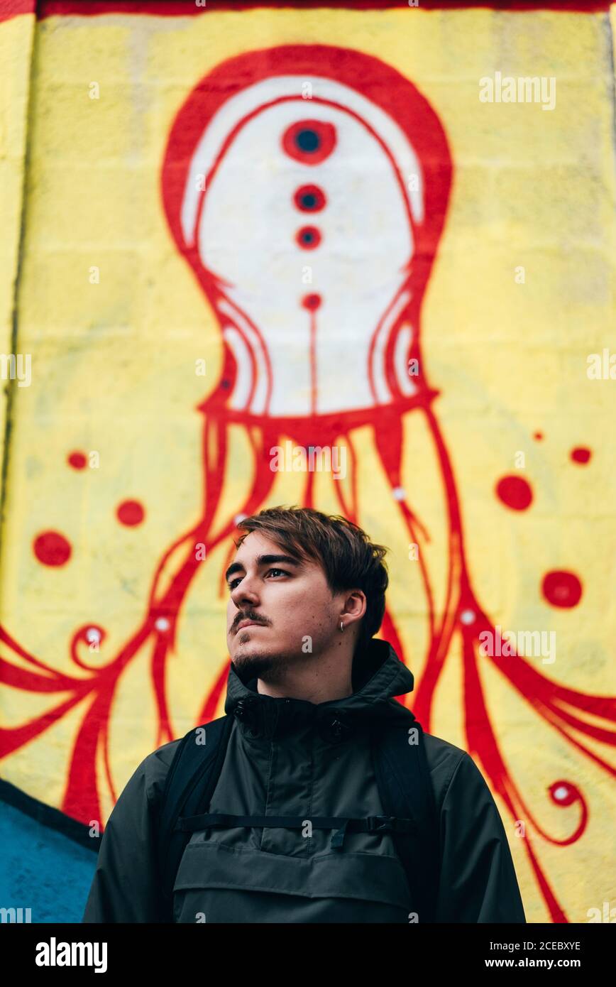 Thoughtful young man standing at graffiti wall with hands in pockets. Stock Photo