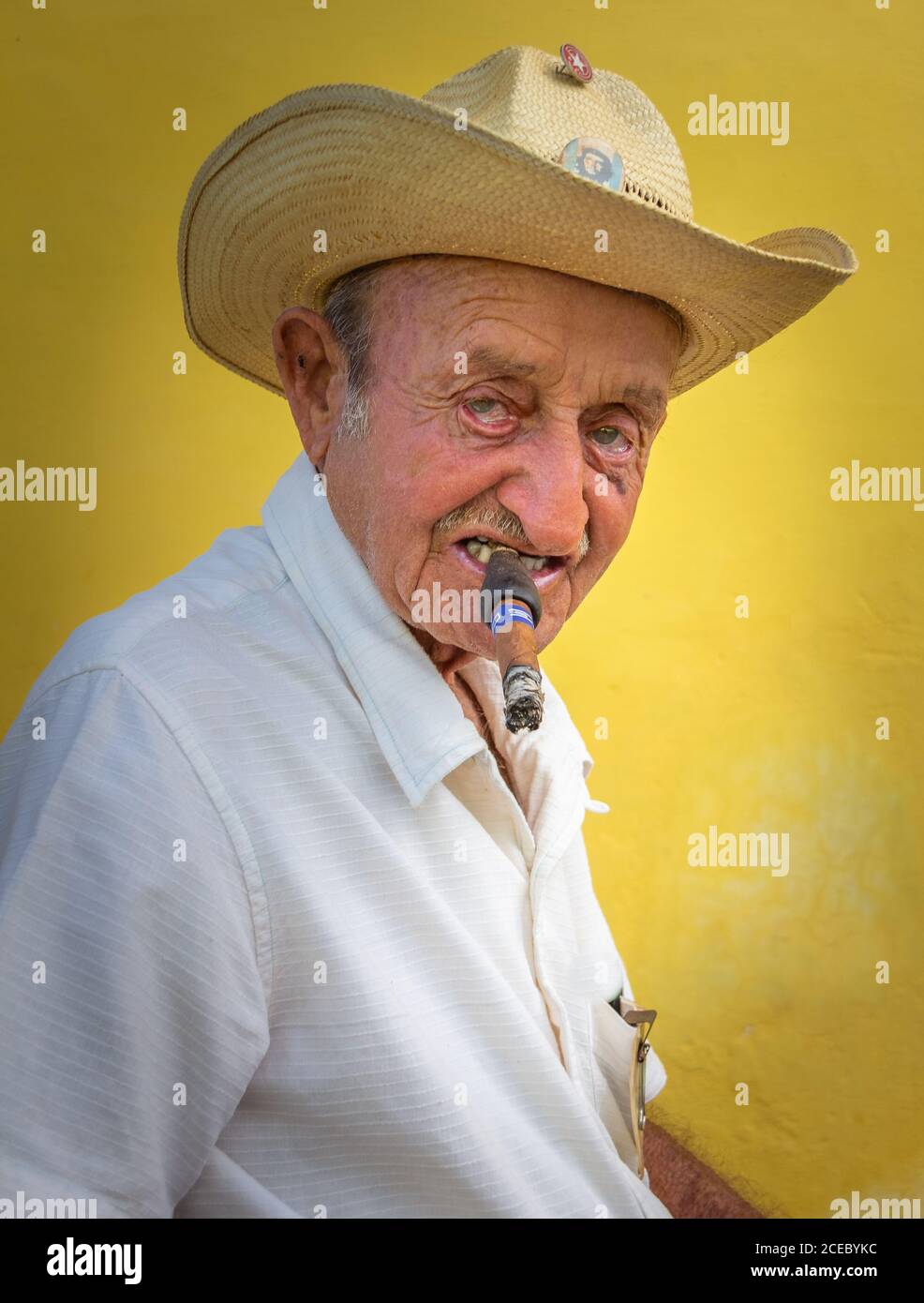 Havana, Cuba - November, 22 2012: Senior male in hat smoking cigar and looking at camera on background of yellow wall on city street Stock Photo