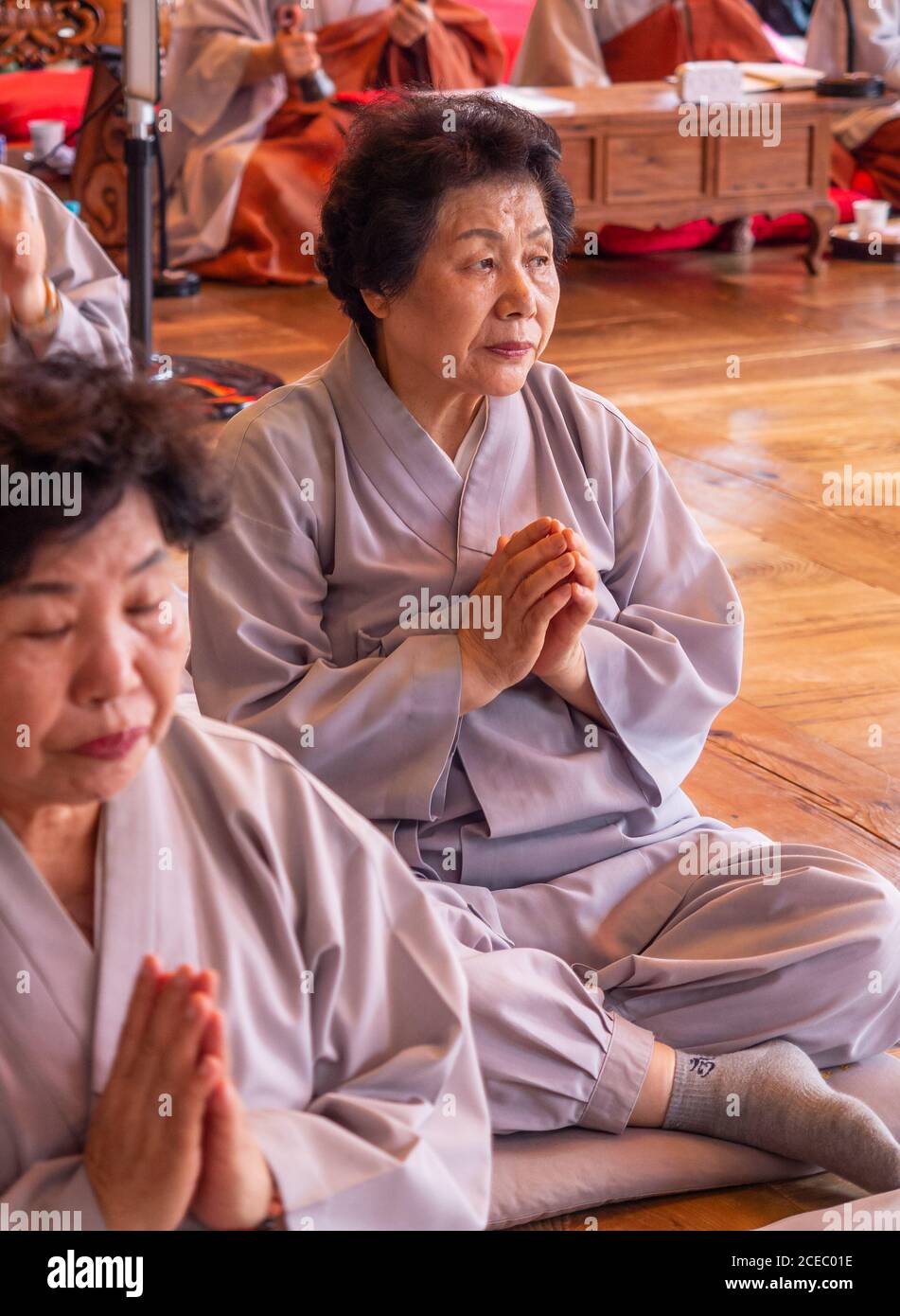 Seoul, South Korea - August, 08 2017: Senior Asian females in traditional clothing clasping hands and praying while sitting on floor in temple Stock Photo