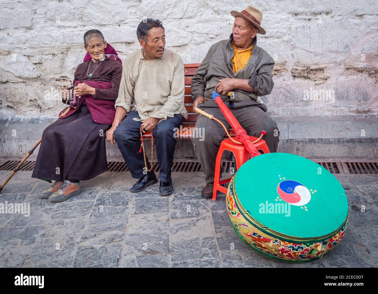 Tibet - August, 29 2014: Ethnic man and woman with beads looking at male with musical instrument while sitting on bench on town street Stock Photo