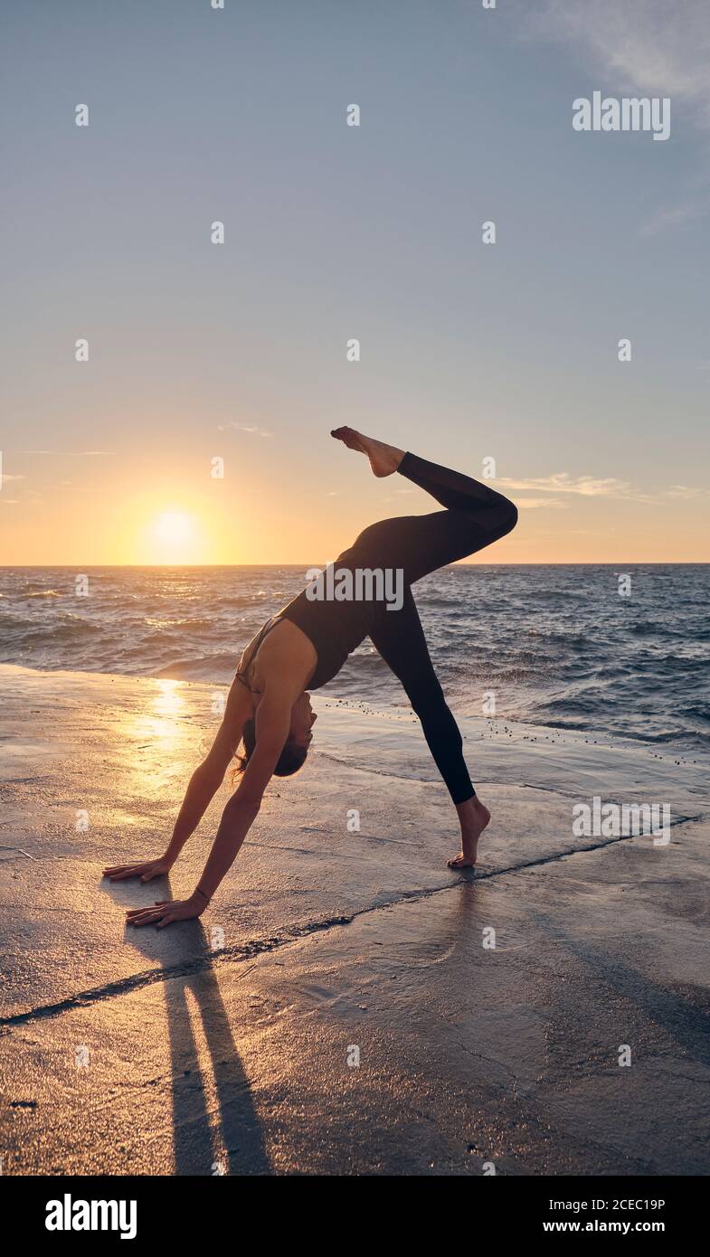 Young Woman in Downward Facing Dog Pose near sea Stock Photo
