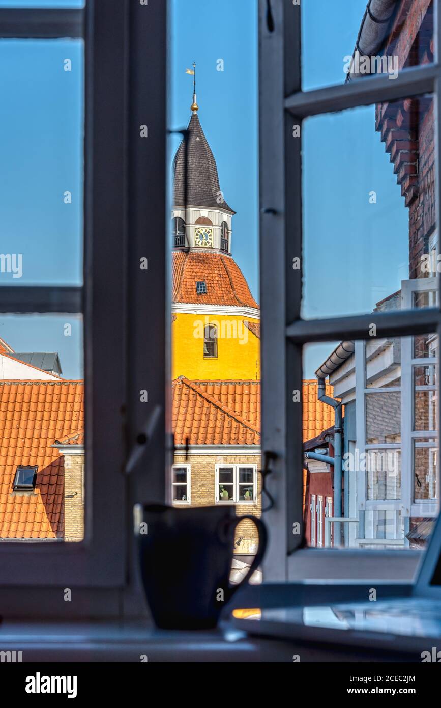a coffee mug and a laptop standing in the window frame and a church tower in the background, Faaborg, Denmark, August 15, 2020 Stock Photo