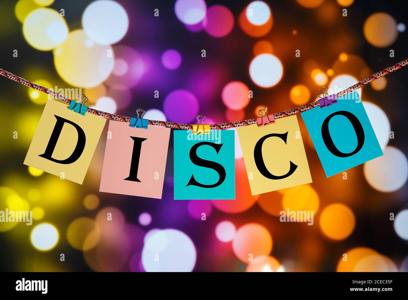 The letters DISCO sign hanging on a clothespin on a background of multi-colored lights. Stock Photo