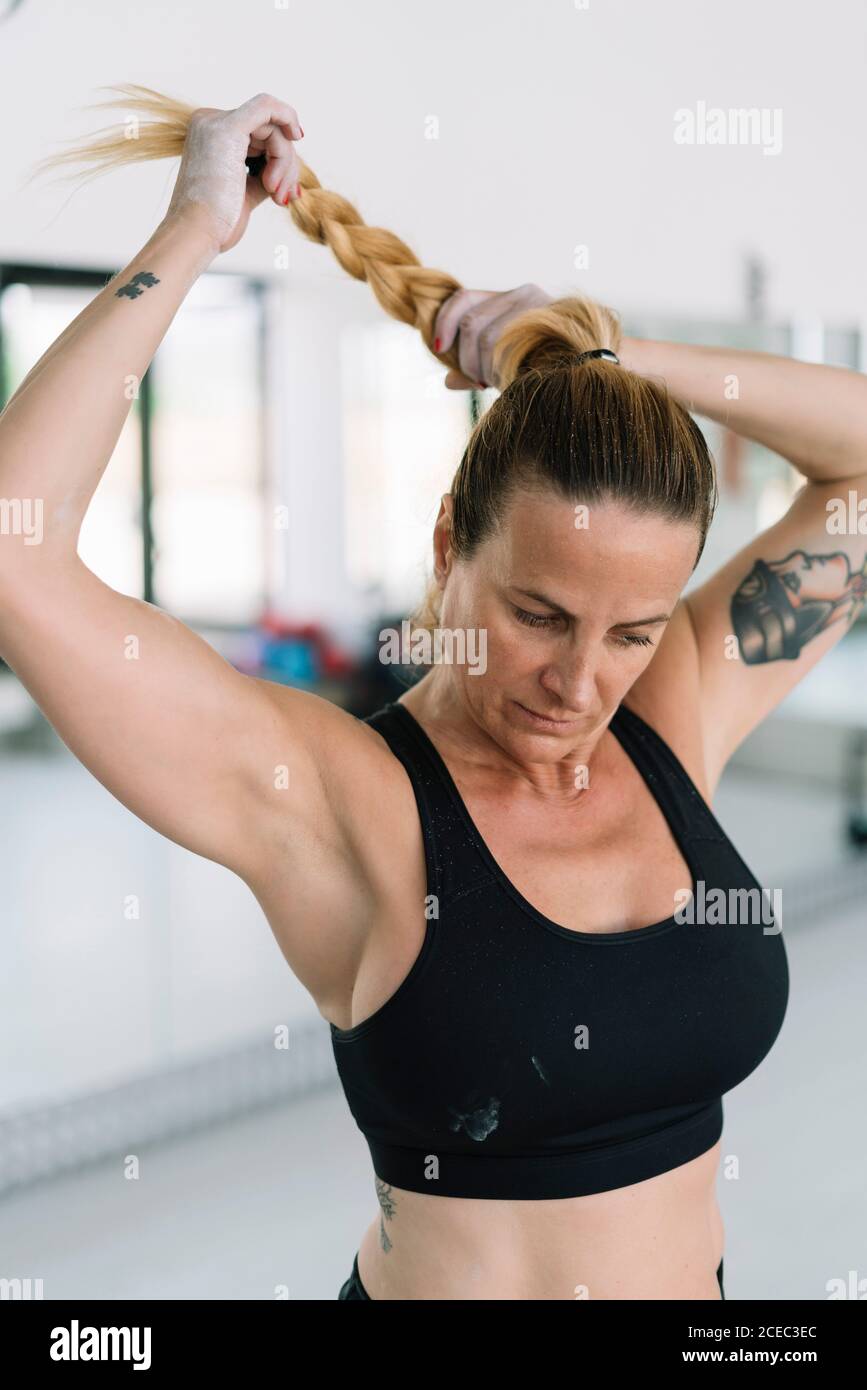 Beautiful adult female in sports bra making braid while training in gym  Stock Photo - Alamy