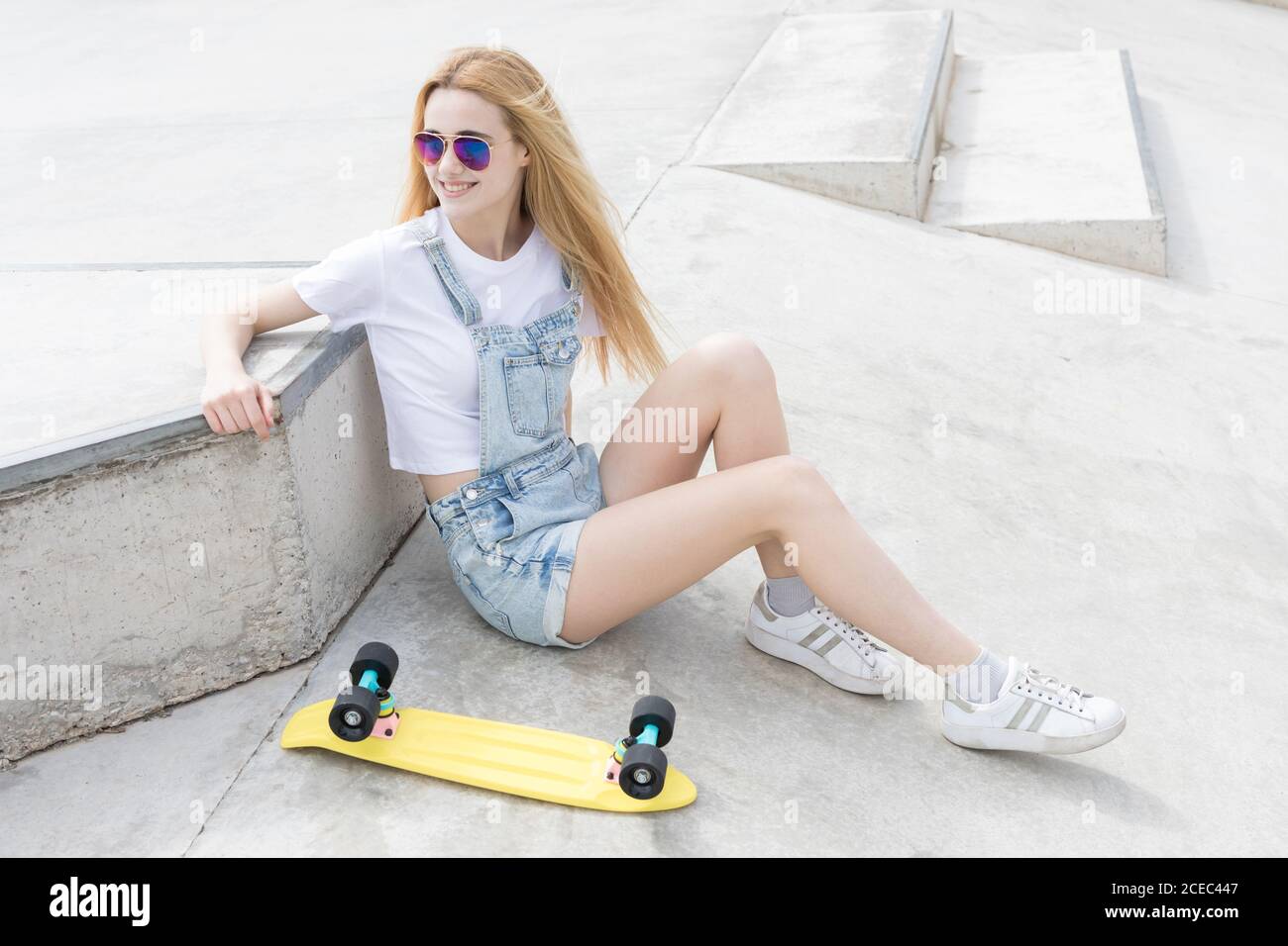 Blonde girl sitting on floor with penny board Stock Photo - Alamy