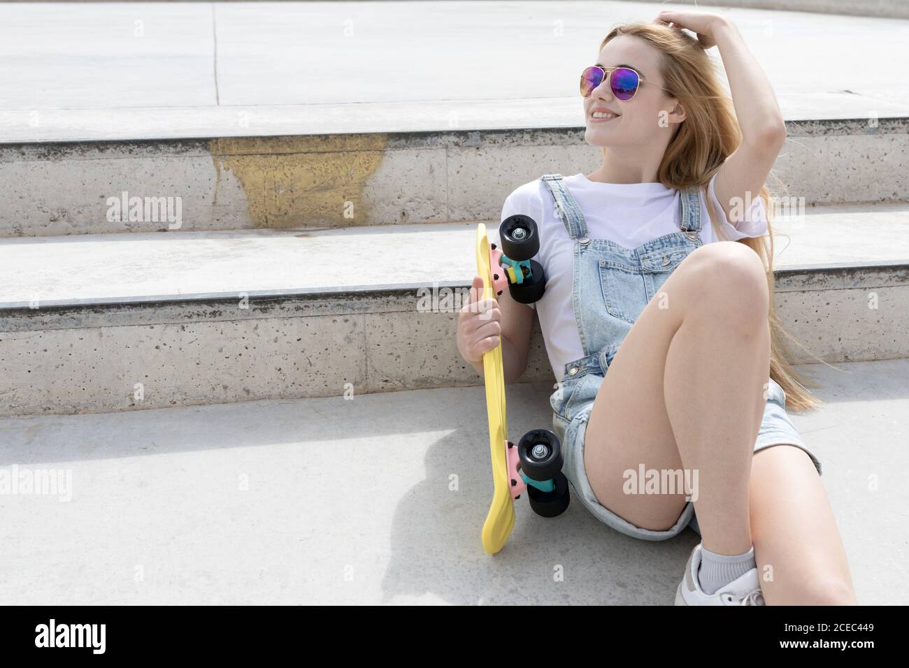Blonde girl sitting on floor with penny board Stock Photo - Alamy