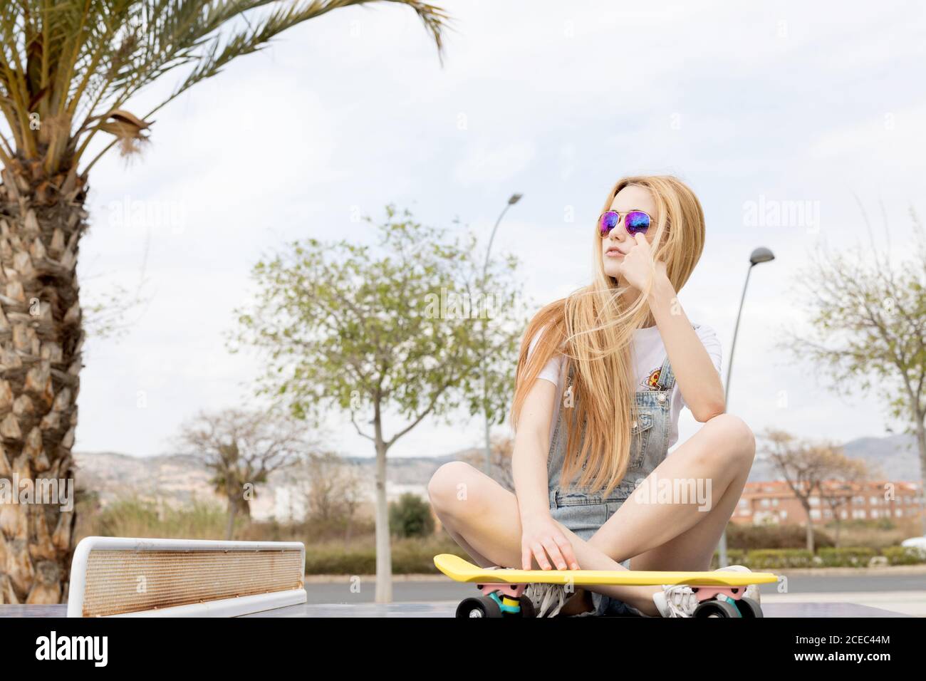 Blonde girl sitting on floor with penny board Stock Photo - Alamy