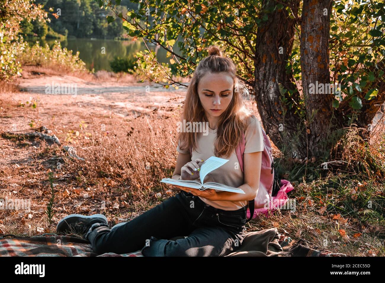 Young girl, student sitting outdoor with backpack and reading a book. Study from home. Cottagecore Stock Photo