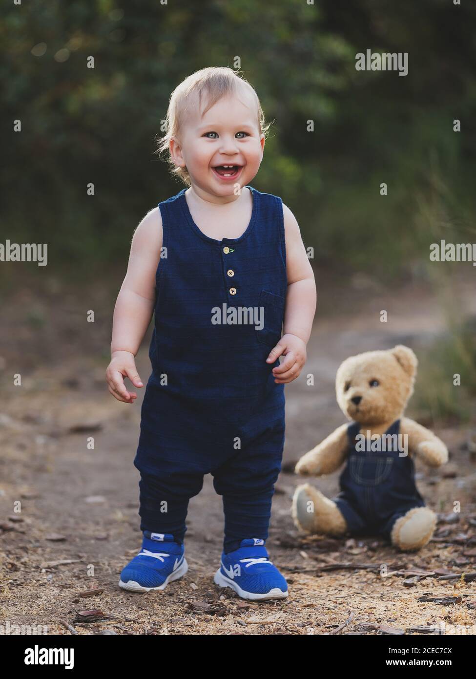 Cheerful little boy standing at bear toy in denim clothes in nature. Stock Photo