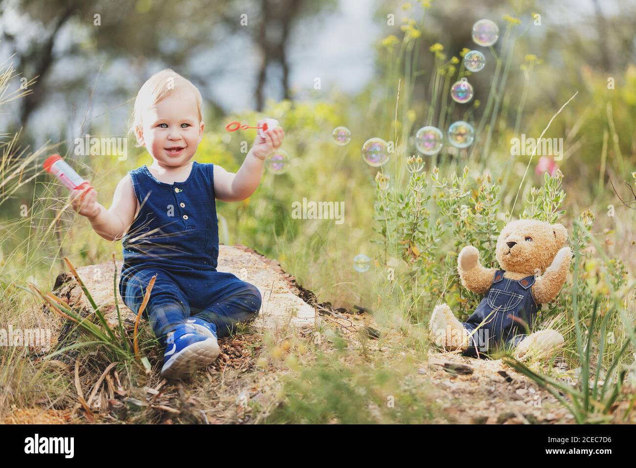 Cheerful little boy standing at bear toy in denim clothes in nature. Stock Photo