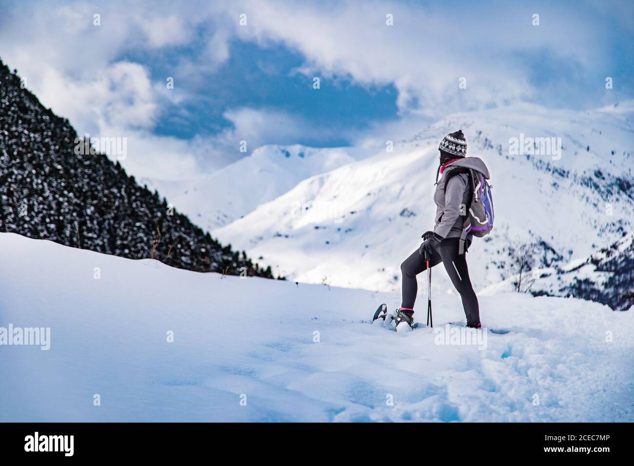 Side view of female in warm clothes lifting leg with ski while standing on snowy mountain slope Stock Photo